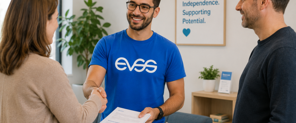 Smiling male support worker in blue EVSS branded shirt shaking hands with a female client while a male client looks on in a…